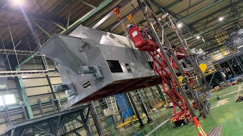 工場内で大型機械設備を設置する作業中の様子。赤い高所作業台と吊り具で位置決め